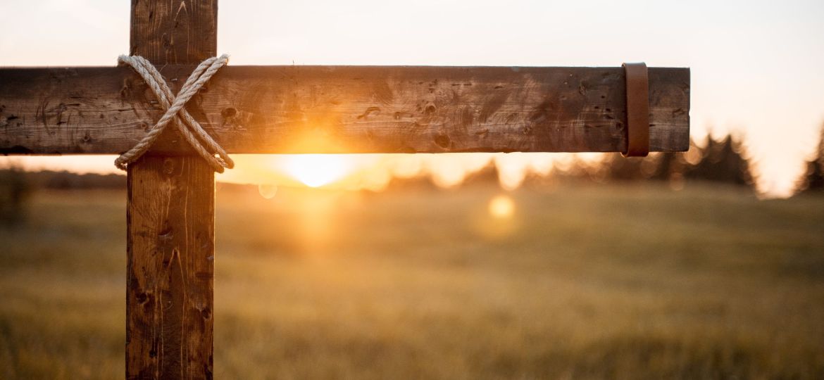 A closeup shot of a wooden cross with the sun shining in the blurred background